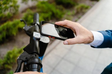 Beyaz adam şehrin caddesinde elektrikli scooterla dururken cep telefonu kullanıyor.
