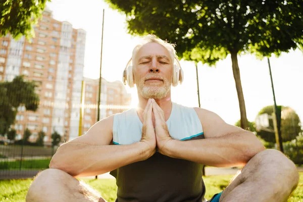 老人在绿地公园练瑜伽时冥想和听音乐 — 图库照片