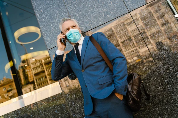 Senior Man Face Mask Talking Mobile Phone While Standing Building — Zdjęcie stockowe
