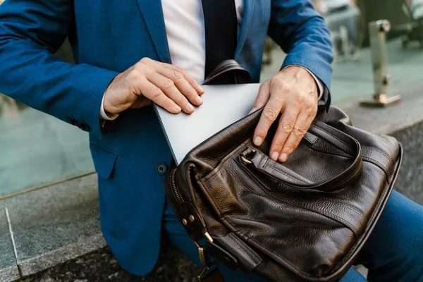 Takım elbise giymiş üst düzey bir adam şehir caddesinde otururken dizüstü bilgisayarla çalışıyor.
