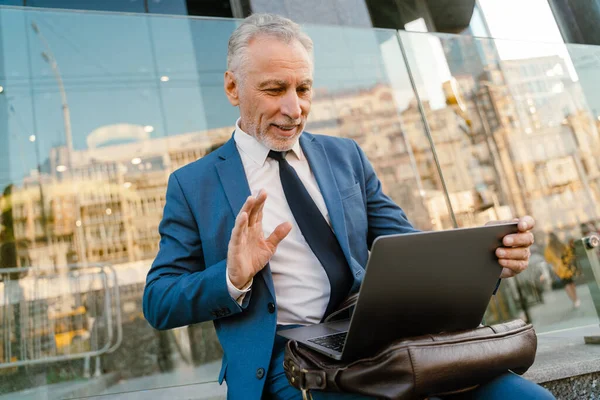 Belediye binasında otururken el sallayan ve dizüstü bilgisayar kullanan kıdemli bir adam.