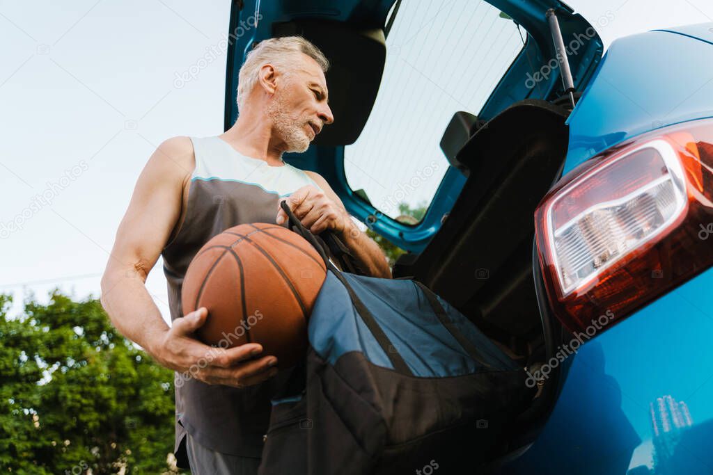 Grey senior sportsman getting ball out of bag in trunk outdoors