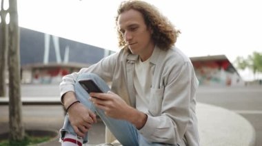 Yakışıklı kıvırcık saçlı adam dışarıda otururken telefonla mesaj atıyor.