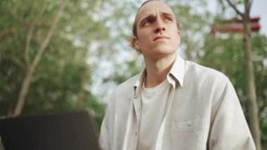 Yakışıklı kıvırcık saçlı adam dışarıda otururken dizüstü bilgisayarda çalışıyor.