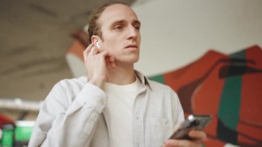 Kulaklıklı, açık havada müzik dinleyen yoğunlaşmış kıvırcık saçlı bir adam.