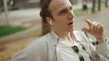 Gülümseyen kıvırcık saçlı adam dışarıda kulaklıkla konuşuyor.