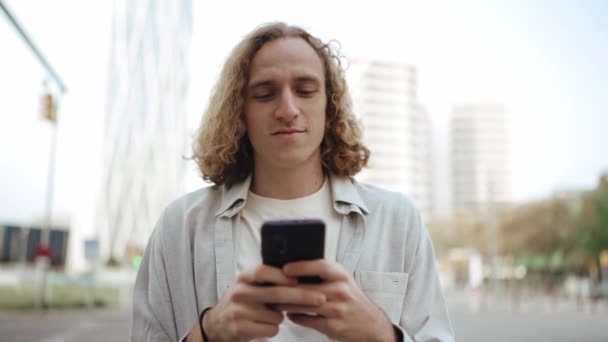 快乐的卷发男子在户外用手机打字 — 图库视频影像