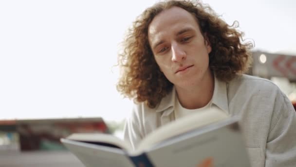 Konsantre Kıvırcık Saçlı Adam Dışarıda Otururken Kitap Okuyor — Stok video