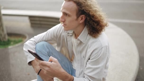 Meditative Curly Haired Man Typing Phone While Sitting Outdoors — Stock video