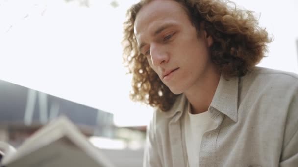 Handsome Curly Haired Man Reading Book While Sitting Outdoors — Vídeo de Stock