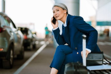 Havaalanı otoparkında oturan gri Asyalı kadın cep telefonuyla konuşuyor.