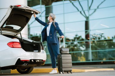 Yüzü maskeli gri Asyalı kadın havaalanının orada bagajı açıyor.