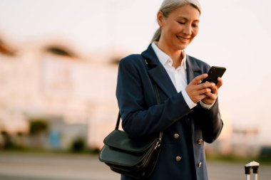 Dışarıda cep telefonu kullanırken gülümseyen gri Asyalı kadın.