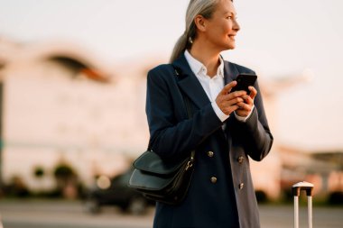 Dışarıda cep telefonu kullanırken gülümseyen gri Asyalı kadın.