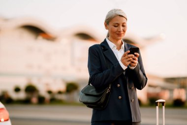 Dışarıda cep telefonu kullanırken gülümseyen gri Asyalı kadın.