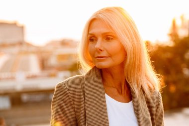 Olgun beyaz iş kadını takım elbise giyiyor poz veriyor ve dışarı bakıyor.