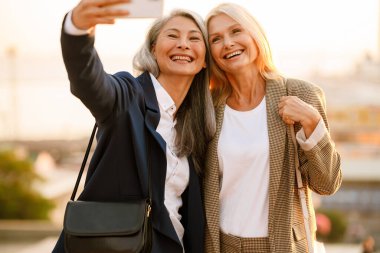 Olgun çok ırklı iş kadınları açık havada buluşurken cep telefonlarıyla selfie çekiyorlar.