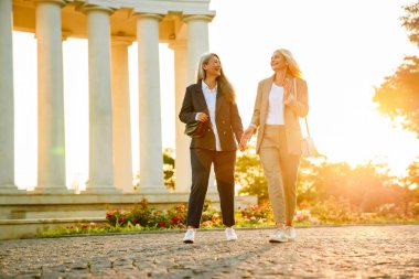 Olgun, çok kültürlü iş kadınları dışarıda yürürken gülümsüyor ve konuşuyor.