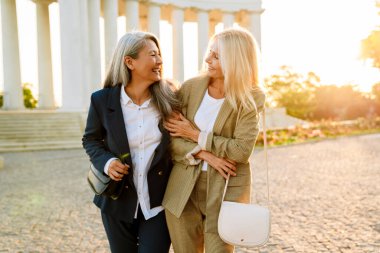 Dışarıda yürürken gülümseyen ve sarılan çok kültürlü iş kadınları.