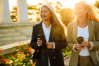 Olgun, çok ırklı iş kadınları dışarıda yürürken kahve içiyorlar.