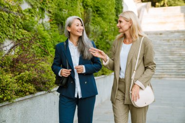 Olgun, çok kültürlü iş kadınları dışarıda yürürken gülümsüyor ve konuşuyor.