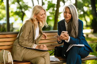 Parkta çalışırken cep telefonu kullanan çok kültürlü iş kadınları.