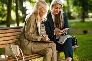 Parkta çalışırken cep telefonu kullanan çok kültürlü iş kadınları.