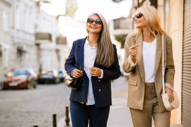 Şehir caddesinde yürürken gülümseyen ve konuşan çok kültürlü kadınlar.