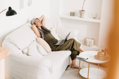 Evde dizüstü bilgisayarla çalışan olgun Asyalı kadın dinleniyor.