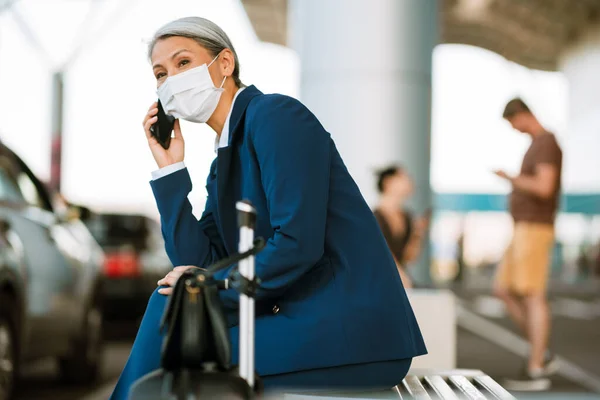 Havaalanının Yanındaki Bankta Otururken Cep Telefonuyla Konuşan Maskeli Gri Kadın — Stok fotoğraf