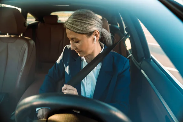 Mature Asian Woman Using Earphone Fastening Seat Belt While Sitting — Foto Stock