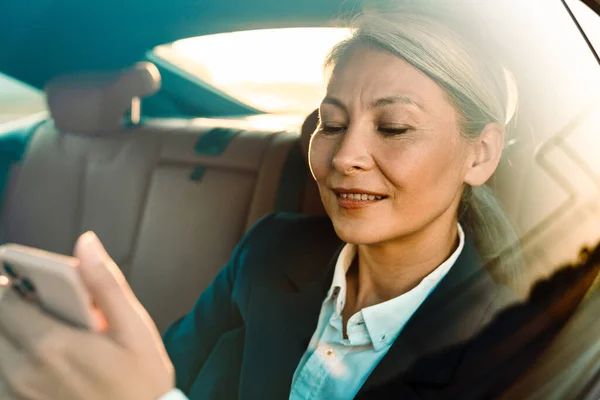 Mature Asian Businesswoman Using Mobile Phone While Going Car — ストック写真