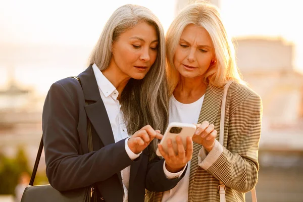 Açık havada buluşurken cep telefonu kullanan çok kültürlü iş kadınları.