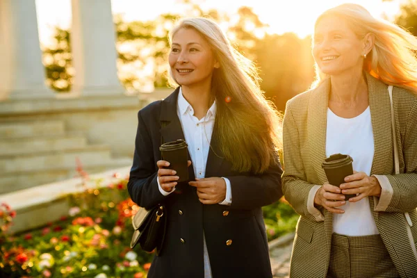 Olgun, çok ırklı iş kadınları dışarıda yürürken kahve içiyorlar.