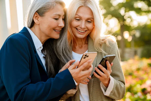 Açık havada buluşurken gülümseyen ve cep telefonu kullanan çok kültürlü iş kadınları.