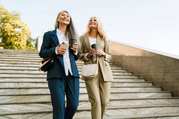 Mature Multiracial Businesswomen Talking Drinking Coffee While Going Stairs Outdoors — ストック写真