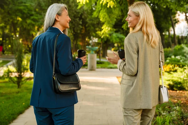 Olgun, çok kültürlü iş kadınları parkta yürürken kahve içiyorlar.