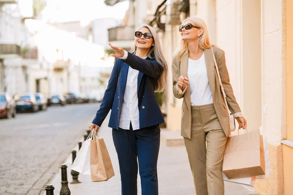 Mature Multiracial Women Talking While Walking Shopping Bags Outdoors — стоковое фото