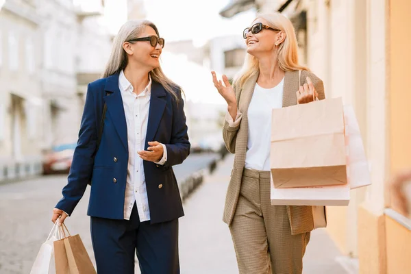 Mature Multiracial Women Talking While Walking Shopping Bags Outdoors — стоковое фото
