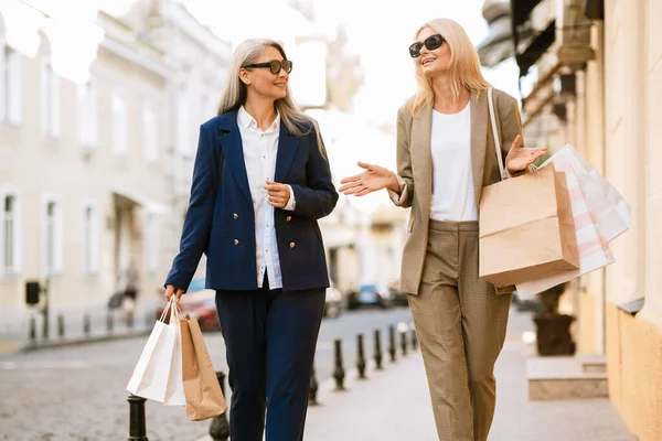 Dışarıda alışveriş torbalarıyla yürürken konuşan çok kültürlü kadınlar.