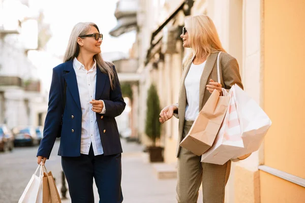 Dışarıda alışveriş torbalarıyla yürürken konuşan çok kültürlü kadınlar.