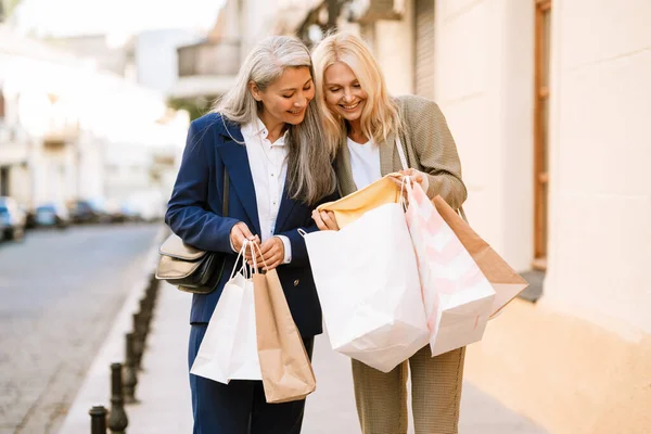 Olgun, çok kültürlü kadınlar dışarıda yürürken alışveriş torbalarına bakıp konuşuyorlar.