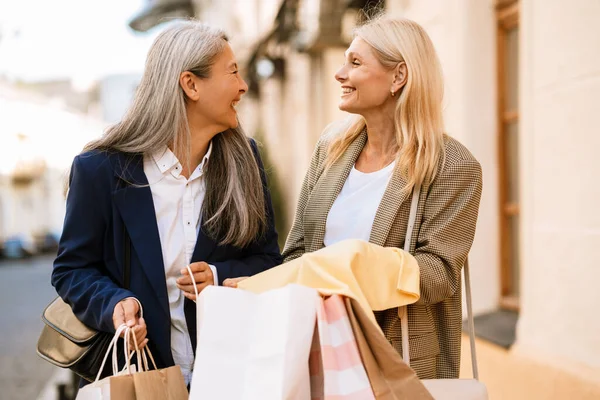 Olgun, çok kültürlü kadınlar dışarıda yürürken alışveriş torbalarına bakıp konuşuyorlar.