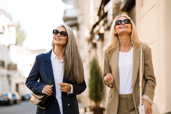 Şehir caddesinde yürürken gülümseyen ve konuşan çok kültürlü kadınlar.