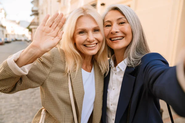 Şehir caddesinde selfie çekerken el kol hareketi yapan olgun kadınlar.