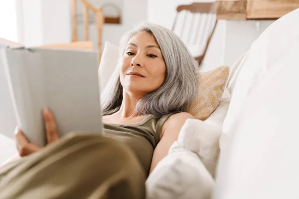 Grey Asian Woman Reading Book While Lying Couch Home — стоковое фото