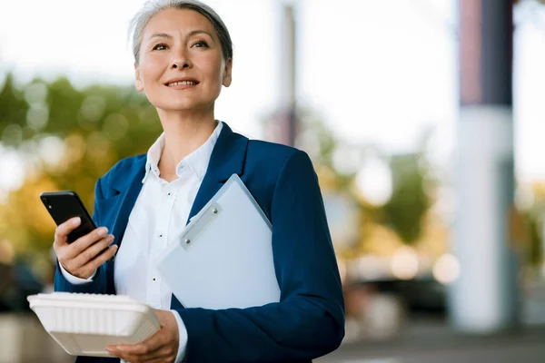 Γκρι Ασιάτισσα Γυναίκα Κρατώντας Κουτί Τροφίμων Και Χρησιμοποιώντας Κινητό Τηλέφωνο — Φωτογραφία Αρχείου