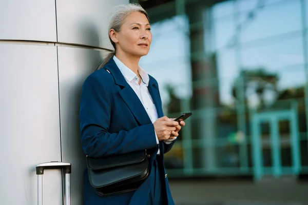Gri Asyalı Kadın Çantasıyla Dışarıda Beklerken Cep Telefonu Kullanıyor — Stok fotoğraf