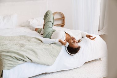 Genç siyahi kadın evde yatarken kulaklıkla müzik dinliyor.