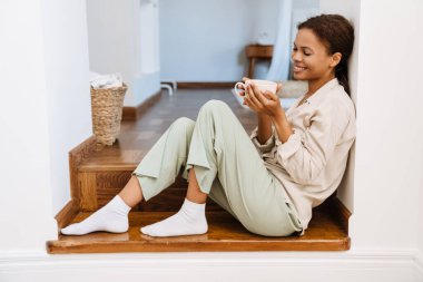 Siyah kadın evde merdivenlerde oturup çay içerken gülümsüyor.